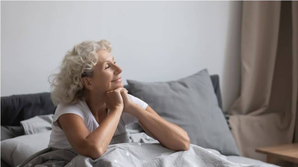 A smiling senior woman in bed after enjoying a good night sleep.