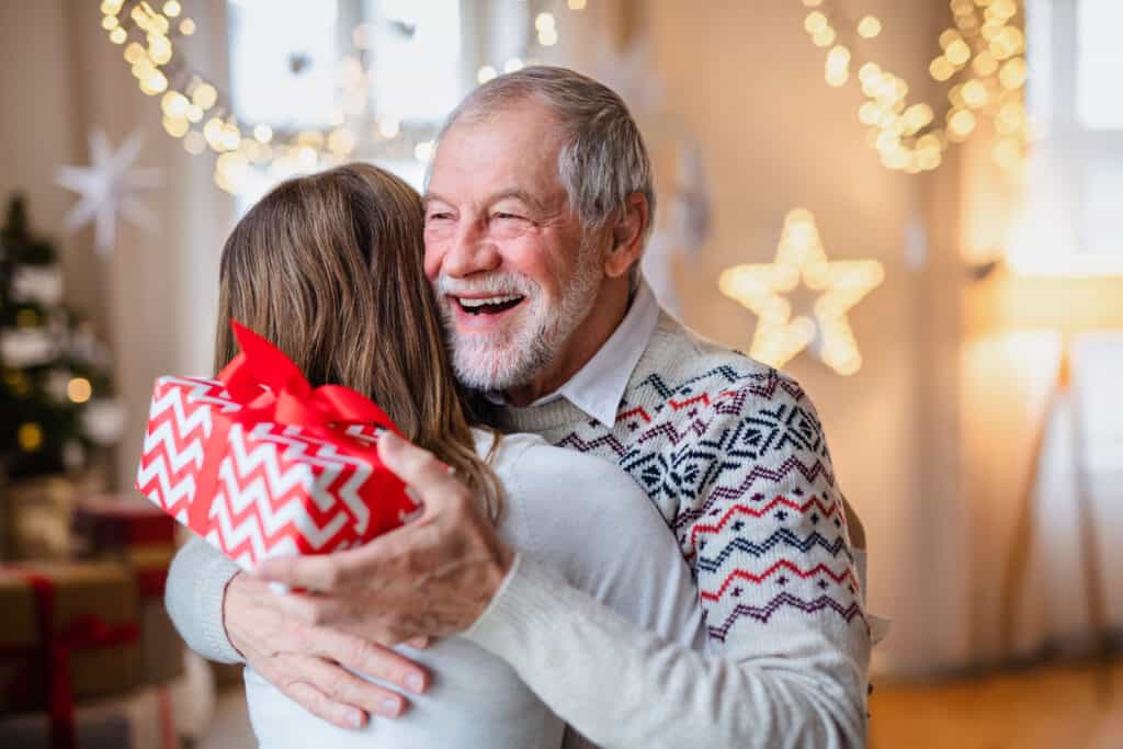 A happy senior man hugging a younger female relative holding a Christmas gift.