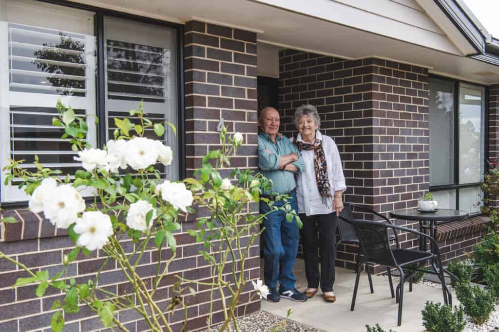 Senior couple standing proudly in the doorway of their Oak Tree Retirement Village home.