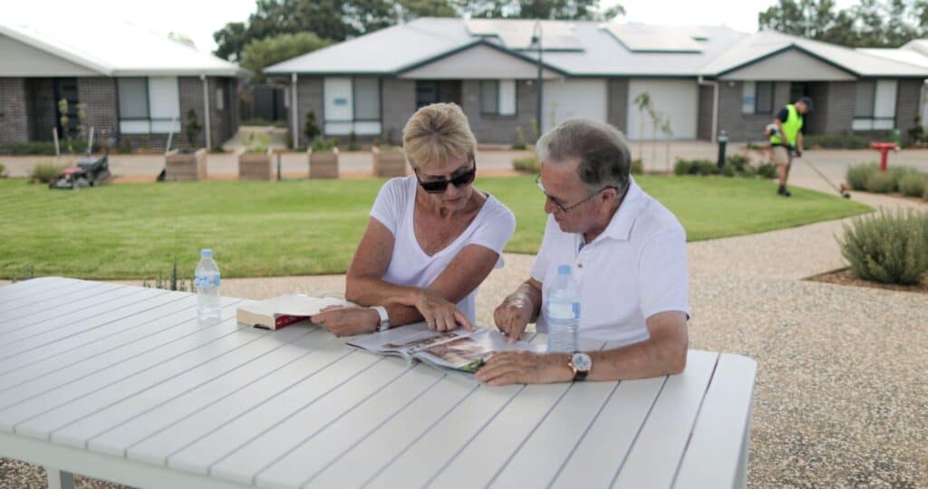 Senior couple sitting in an outdoor communal space in one of our Oak Tree Retirement villages looking at a magazine together.