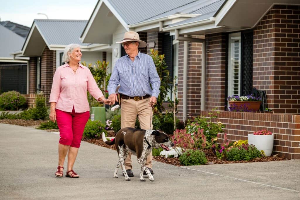 Senior couple and their dog strolling around one of our Oak Tree Retirement Villages enjoying retired life together.