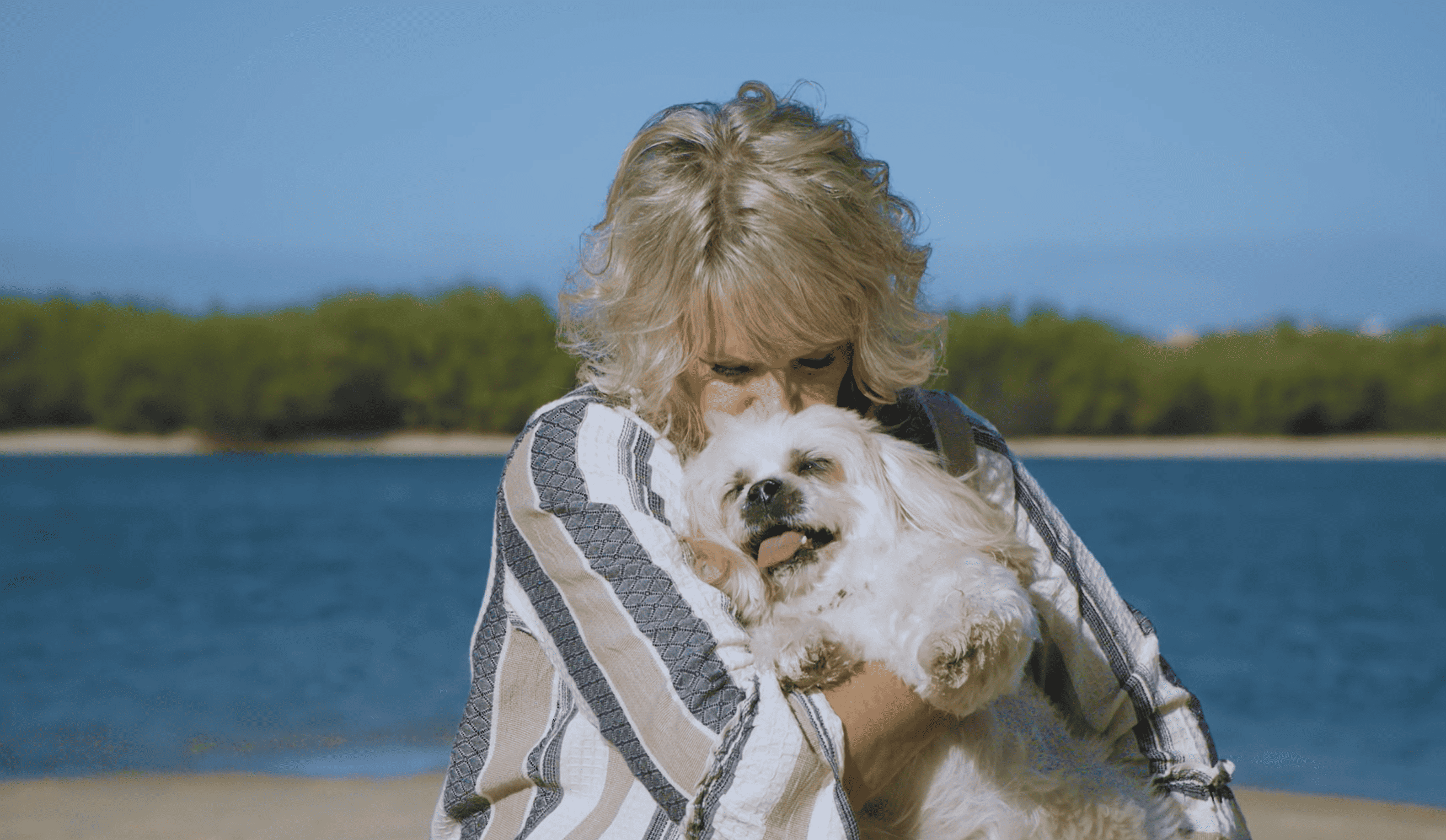 Senior woman hugging her dog with the sea in the background.