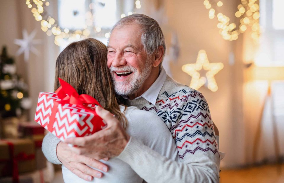 Young,Woman,Giving,Present,To,Happy,Grandfather,Indoors,At,Home