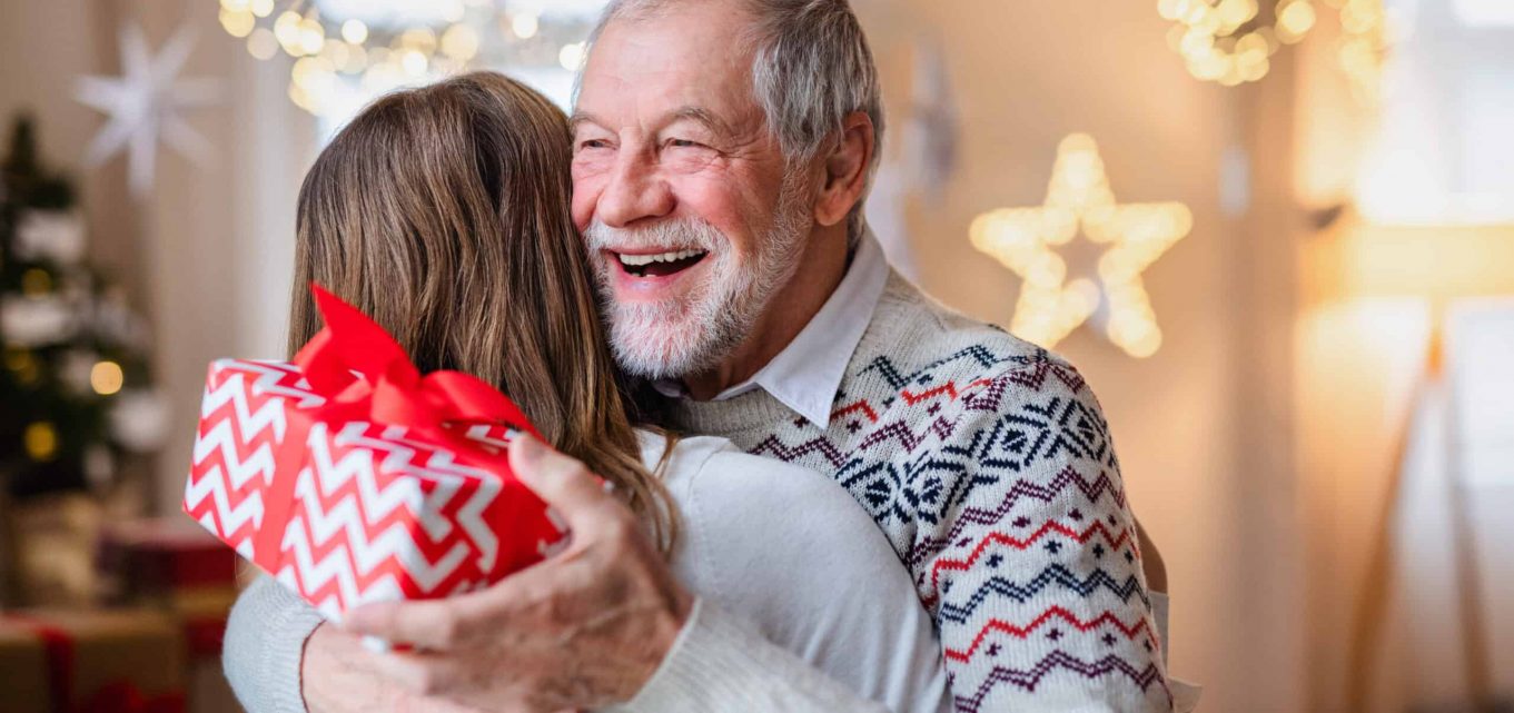 A happy senior man hugging a younger female relative holding a Christmas gift.