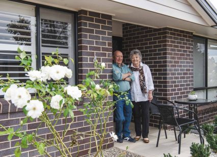 Senior couple standing proudly in the doorway of their Oak Tree Retirement Village home.