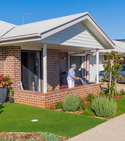 A senior woman watering the plants in the garden of her Coffs Harbour retirement home.