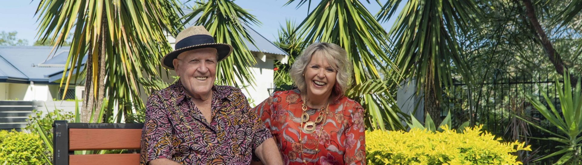 Senior couple sitting on a bench outside surrounded by plants enjoying life at one of our Oak Tree Retirement Village Locations.