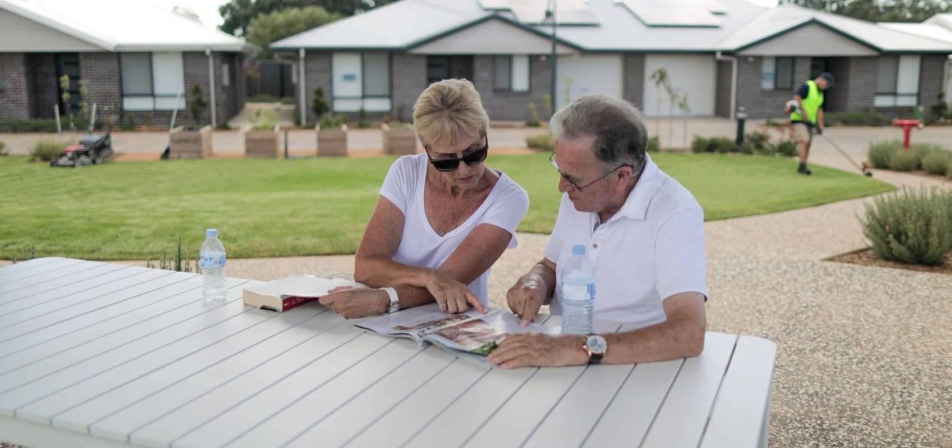 Senior couple sitting in an outdoor communal space in one of our Oak Tree Retirement villages looking at a magazine together.