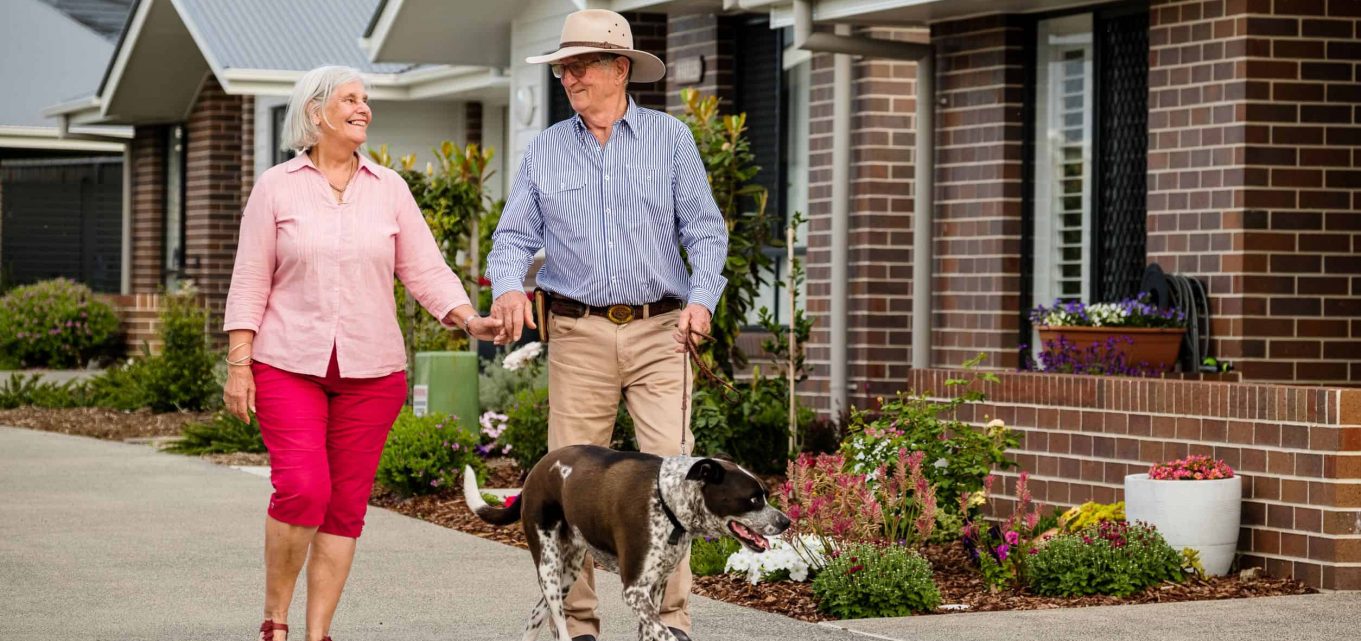 Senior couple and their dog strolling around one of our Oak Tree Retirement Villages enjoying retired life together.