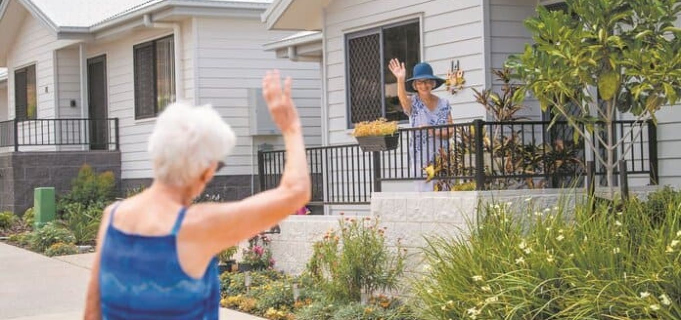 Two older women waving at each other from across the way in one of our Oak Tree Retirement Villages