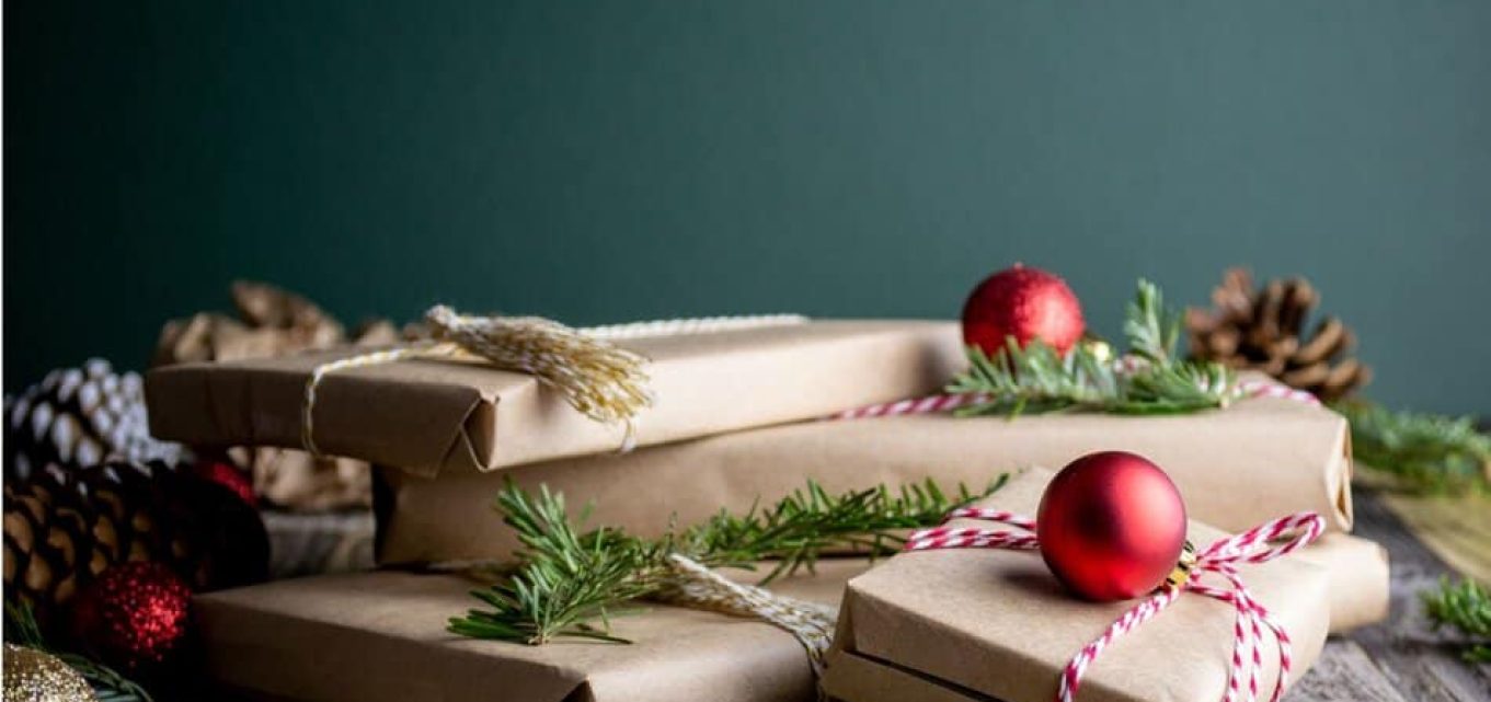 Presents wrapped in brown paper and arranged aesthetically with red baubles and twigs of Christmas tree.