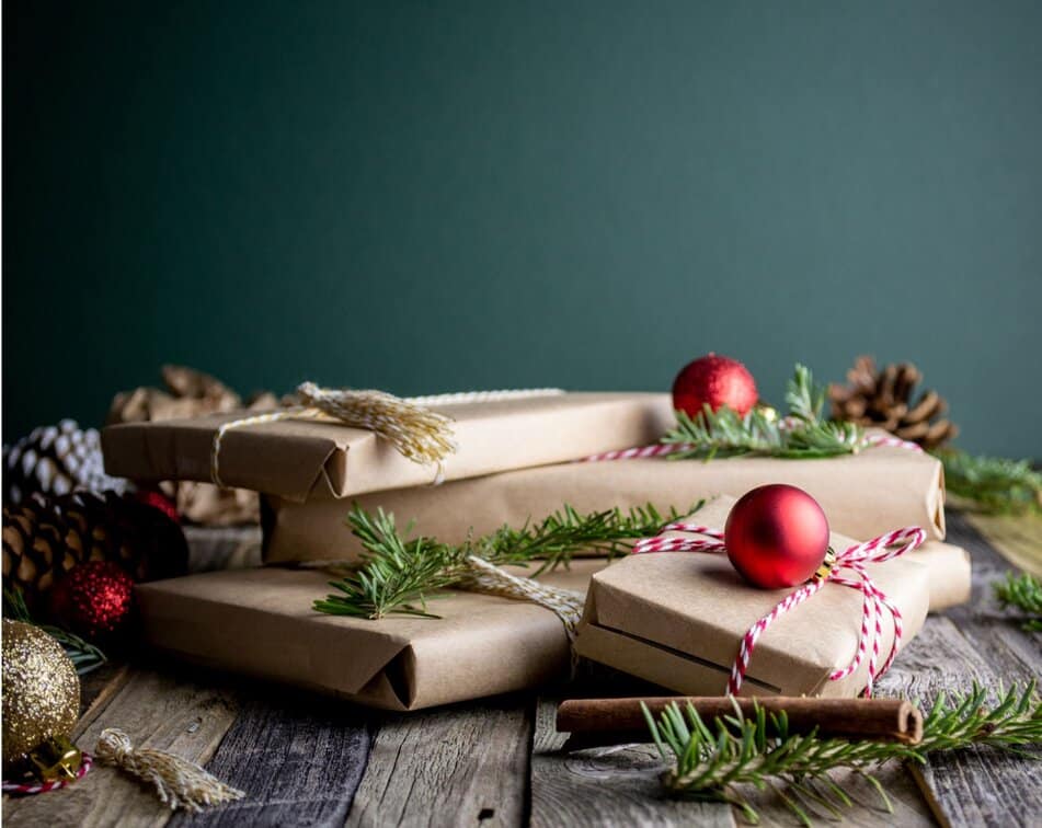 Presents wrapped in brown paper and arranged aesthetically with red baubles and twigs of Christmas tree.